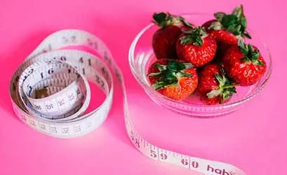 Une assiette en verre contenant des fraises fraîches, accompagnée d'un ruban à mesurer.