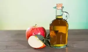 Une composition sur table : une pomme et une bouteille de vinaigre de cidre.